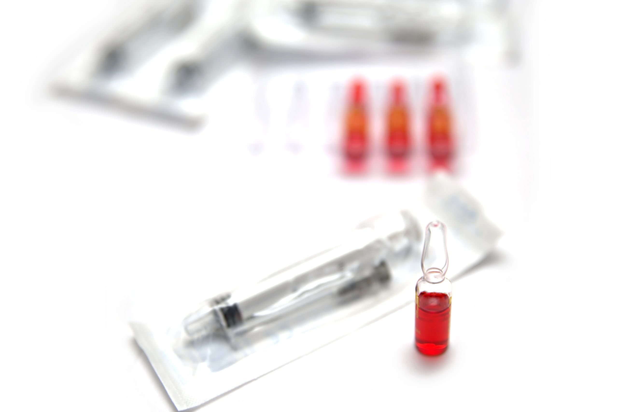 Medical ampoules and syringes with red liquid on white background.