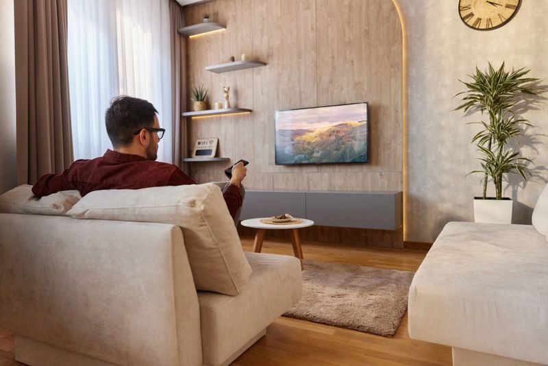 Rear view of carefree man watching TV while relaxing on sofa in the living room.