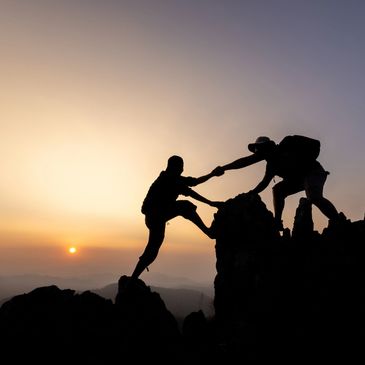 Two hikers helping each other climb rocks at sunset.