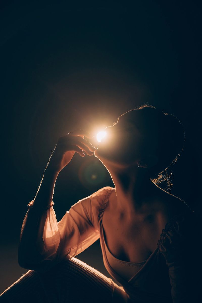 Portrait of young tired ballerina sitting and relaxing after rehearsal against background of the spotlight. Graceful beautiful ballerina. Ballet art, grace, flexibility, motion. Backlight.
