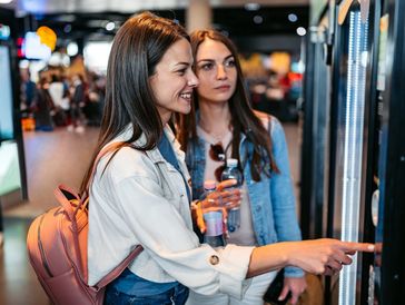 Zwei Frauen benutzen einen Ticketautomaten.