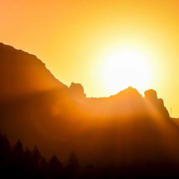 Sun setting behind rugged mountain peaks with golden light.