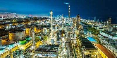 Night view of a large industrial refinery complex with lit towers, pipes, and infrastructure.