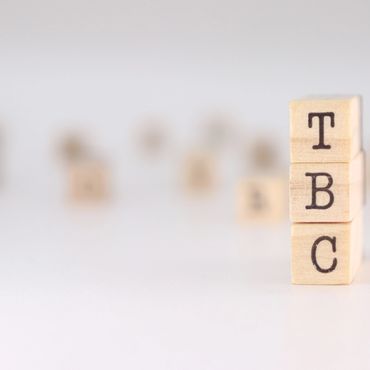 Wooden blocks stacked with letters T, B, and C on a white surface.