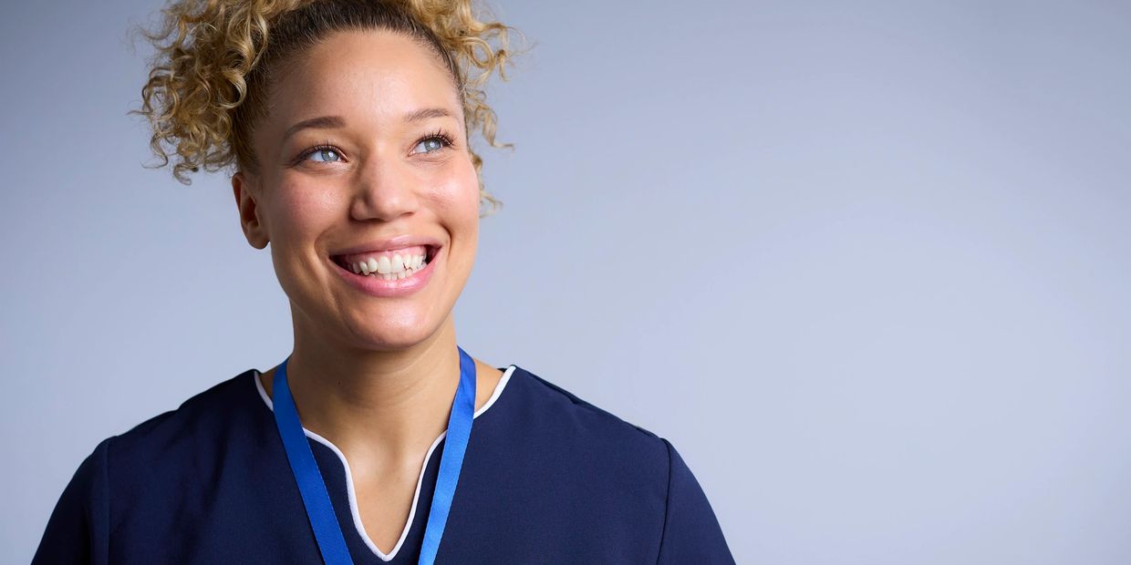 Smiling healthcare worker in uniform with a blue lanyard against a plain background.