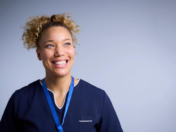 Smiling healthcare worker in navy scrubs with a blue lanyard.