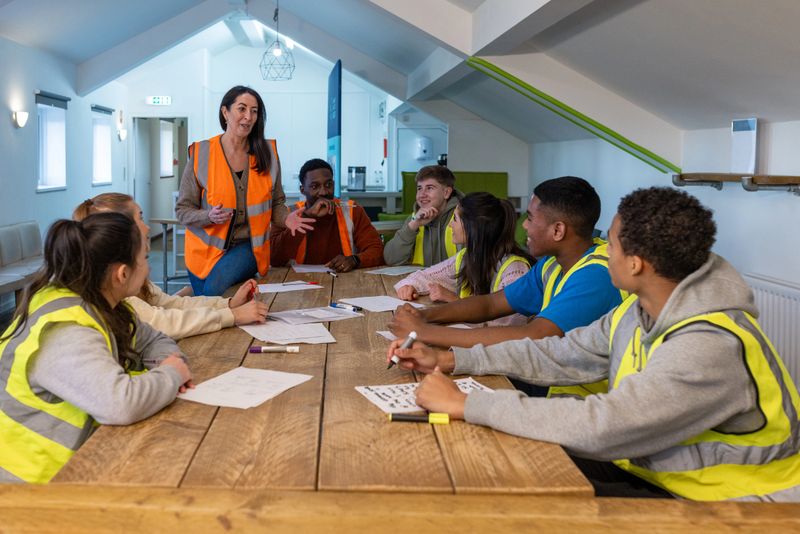 Group of teenagers volunteering at an animal shelter in the North East of England. They are wearing high vis jackets, sitting around a table writing out worksheets being taught by their mentor.