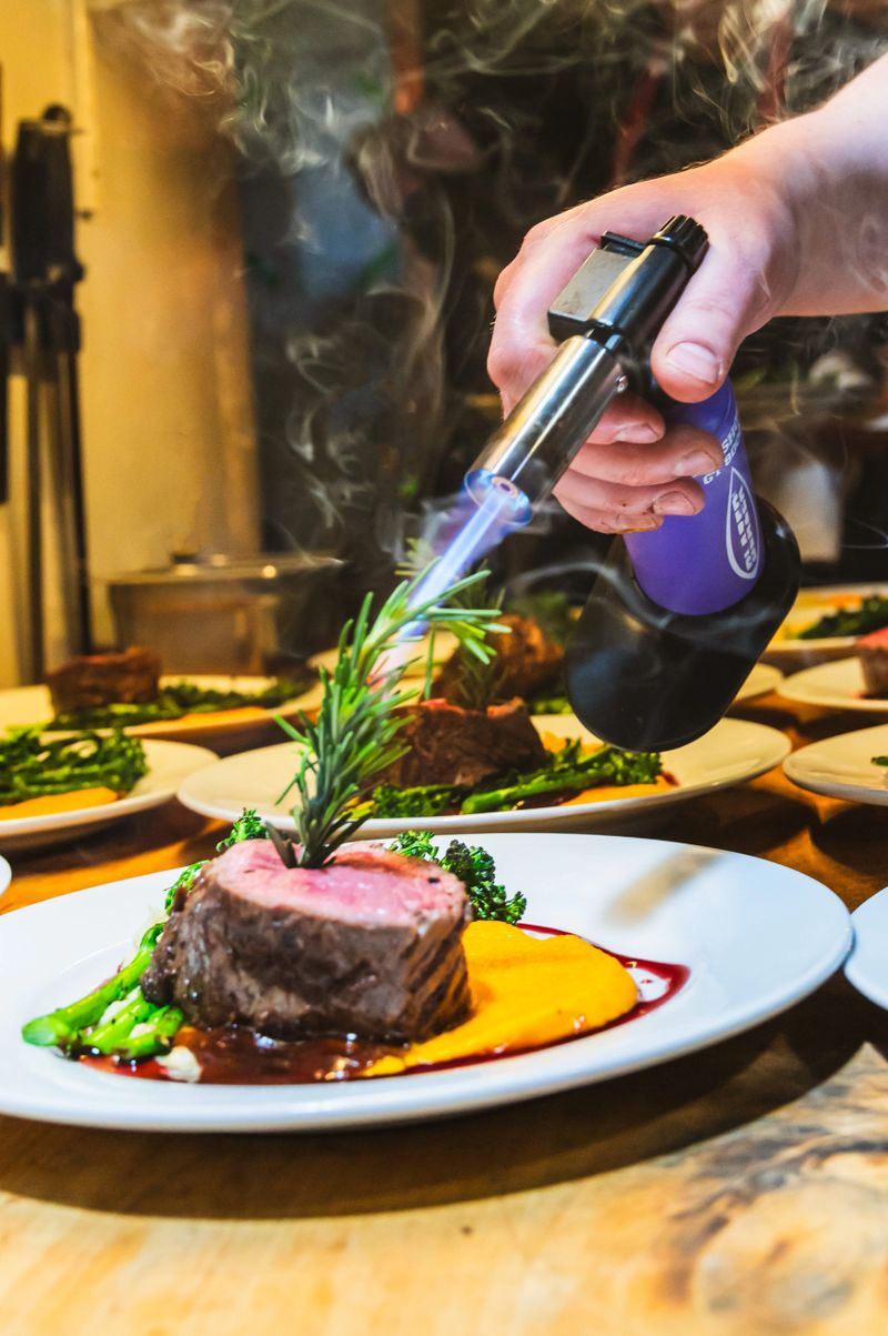 A chef burns then ends of rosemary as the last step to serving steaks in a restaurant.