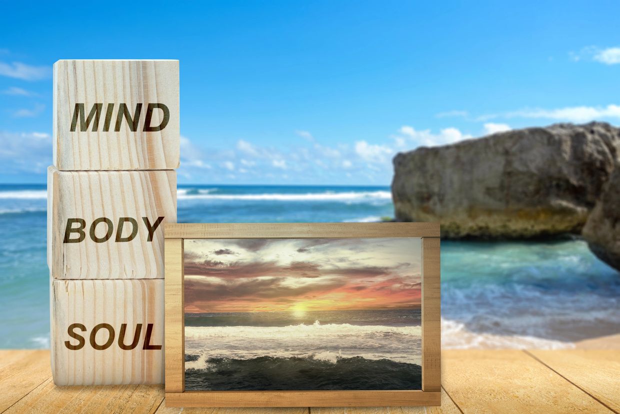 Wooden blocks with mind, body, soul and ocean sunset framed on a beach.