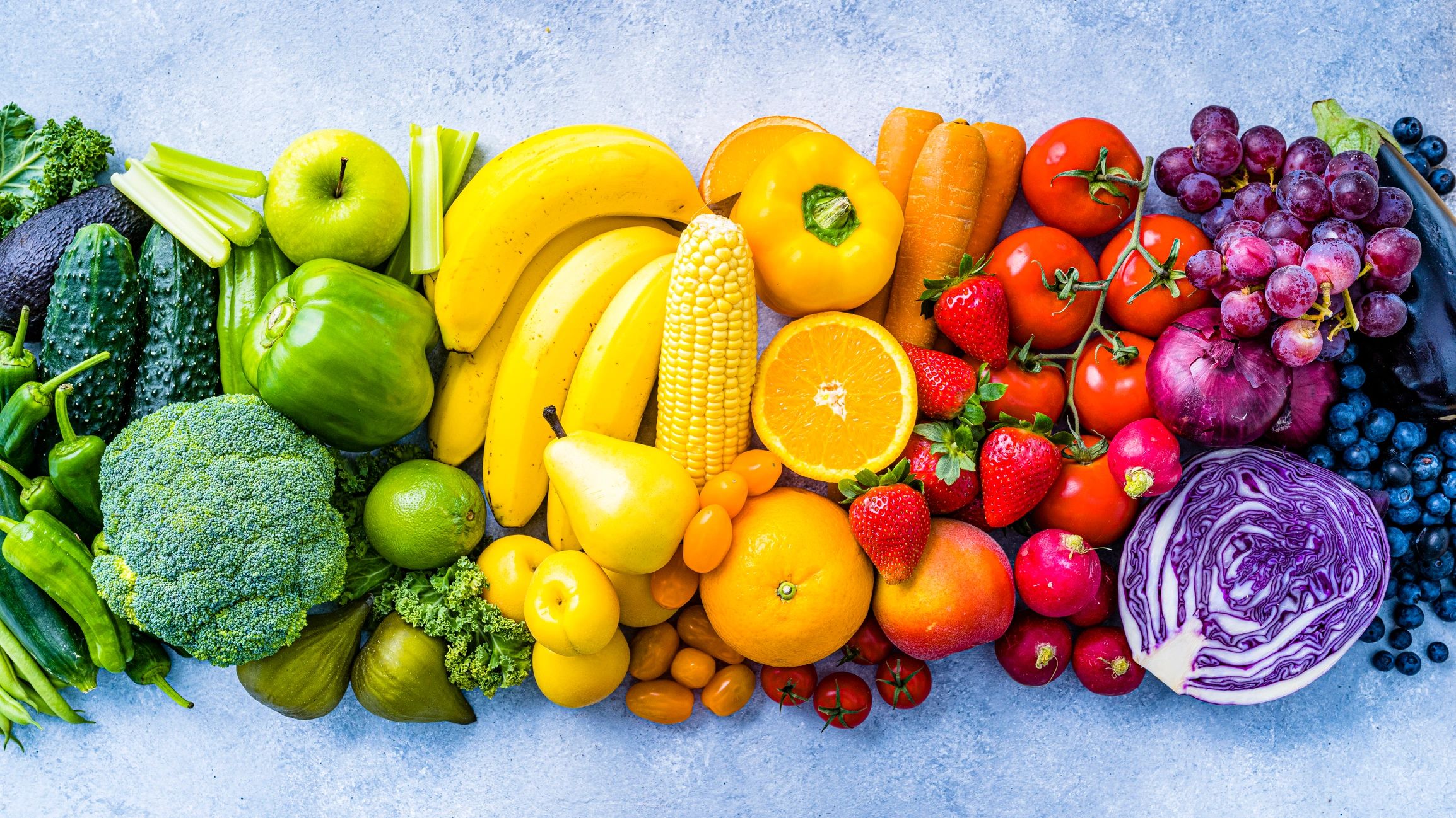 A colorful array of fresh fruits and vegetables arranged by color on a blue surface.