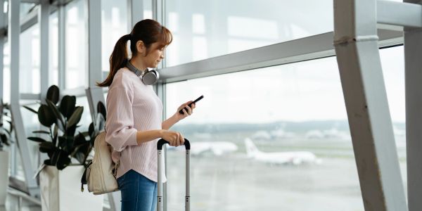 Woman looking at phone while waiting at airport with luggage.