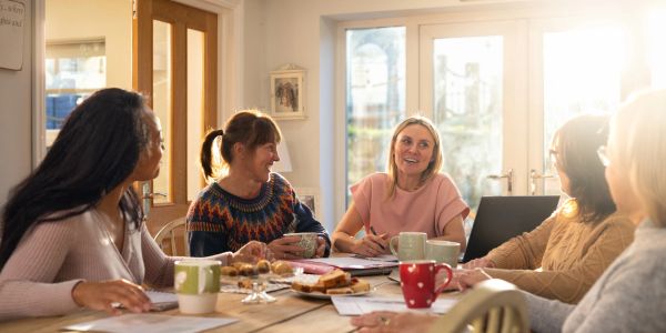 A group of women enjoying a lively meeting around a table with coffee and snacks.
