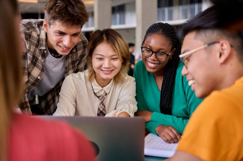 Group of diverse multiethnic smiling young students using laptop studying gathering in classroom. Academics multiracial people classmates working in a project creative inside of university building
