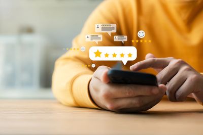 Person giving a five-star rating on a smartphone with review icons around.