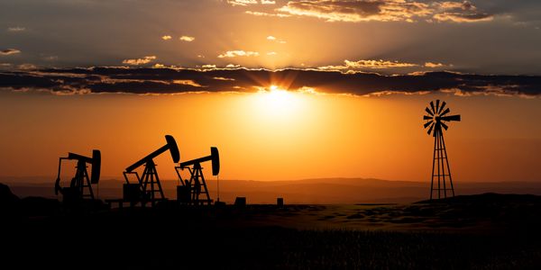 Oil pumps and a windmill silhouette against a vibrant sunset.