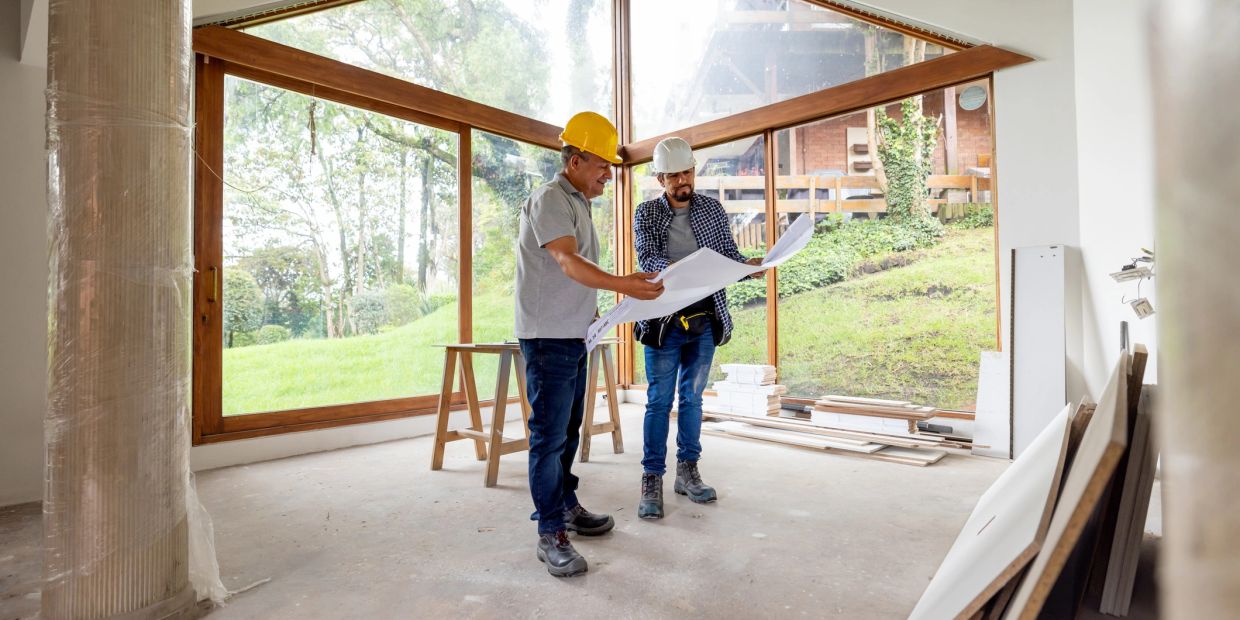 Two construction workers reviewing blueprints inside a modern house under construction.