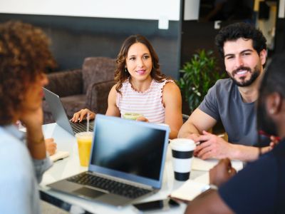 A group of young professionals having a discussion around a table with laptops.