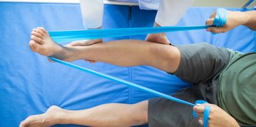Physical therapy session using a blue resistance band for leg rehabilitation.