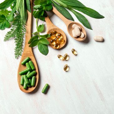 Wooden spoons with herbs and supplements on a white surface.