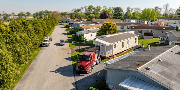 A red truck transporting a mobile home through a residential area with other mobile homes.