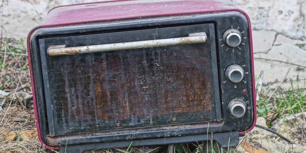 Old, rusty oven toaster left outdoors on the ground.