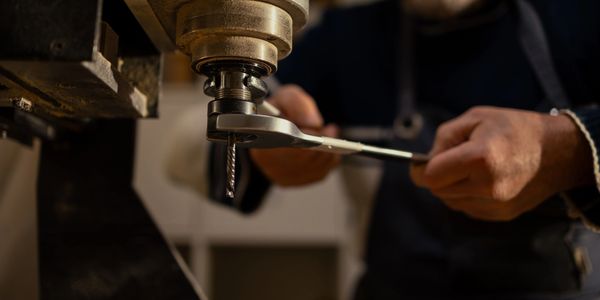 Person adjusting a drill on a machine with a wrench.