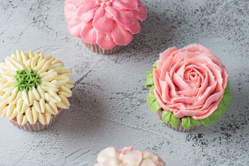 Colorful cupcakes with flower shaped decorations made with buttercream frosting.