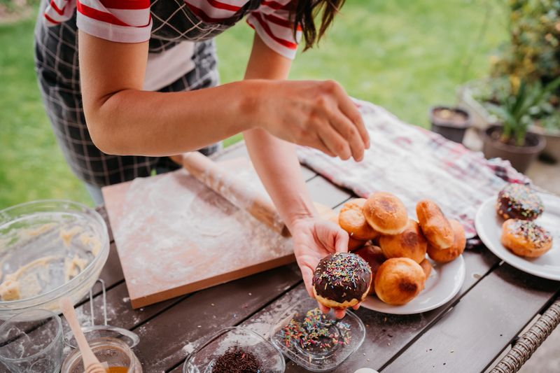 Young woman decorating doughnuts she just made in her garden