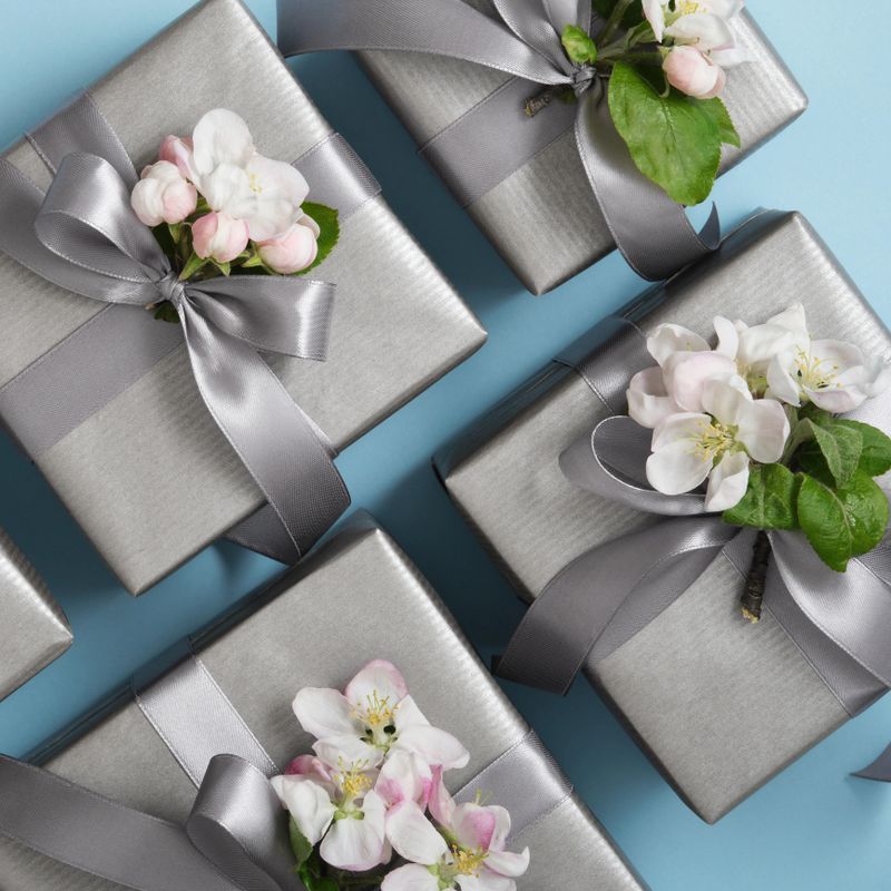 Gray gift boxes with apple flowers and silver ribbons on light blue background.