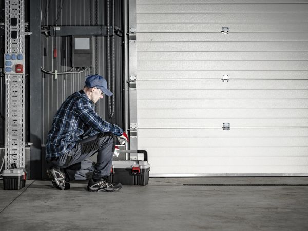 Worker kneeling with toolbox in front of a garage door.