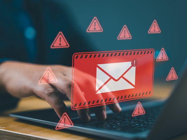Hand typing on a laptop with red warning email icons indicating a security threat.
