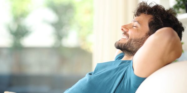 A man relaxing on a couch with a peaceful smile.