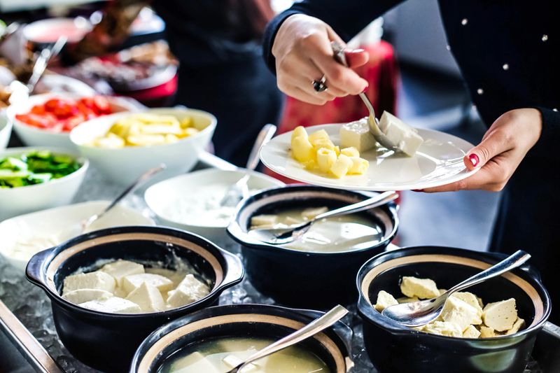 A woman dressed in a uniform is serving various dishes from a buffet table at a catered event.