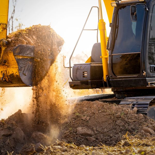 A yellow excavator dumping soil on a construction site.