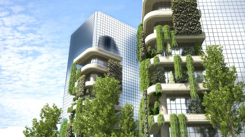 The facade of a modern building incorporates lush greenery, blending urban construction with nature. Balconies with plants wind up the structure, which reflects the sky in its glass surfaces under the bright sunlight of a clear day.