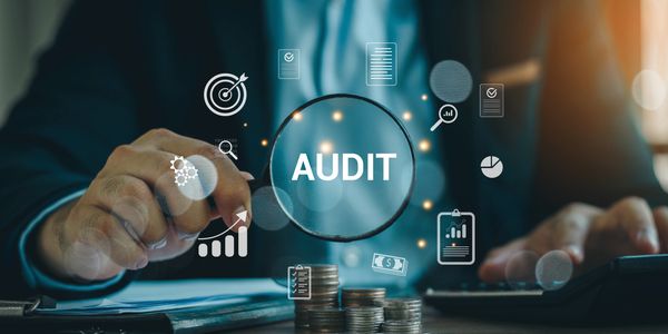 Businessman examining financial data with a magnifying glass labeled 'AUDIT'.