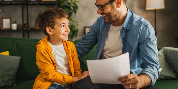 Father and son smiling while looking at a paper together on a couch.