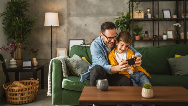 A man and his son sitting on a couch and playing a game in mobile.
