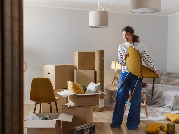 Woman arranging furniture in a room filled with moving boxes.