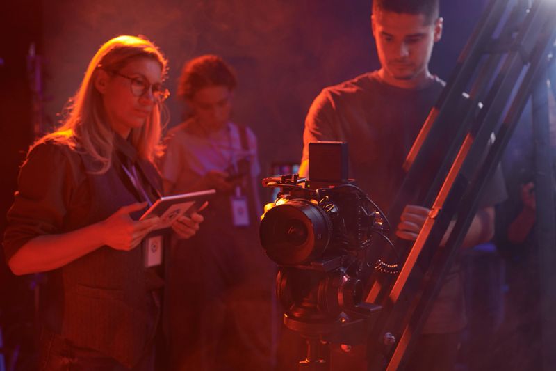 Video production crew working together backstage on set in red neon lights, copy space