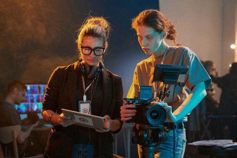 Waist up portrait of two women working in video production crew and looking at digital tablet screen copy space