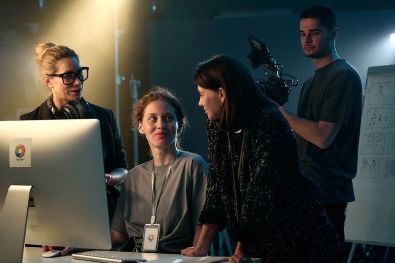Portrait of video production crew reviewing footage and using computer on set smiling