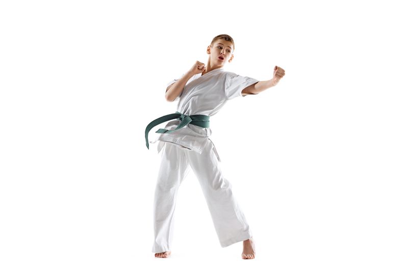 Focused teen boy, karate practitioner showing dynamic kick, illustrating discipline and power isolated on white studio background. Sport, martial arts, combat sport, health, active lifestyle concept