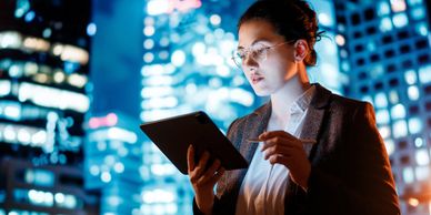 A professional woman using a tablet at night in a cityscape.