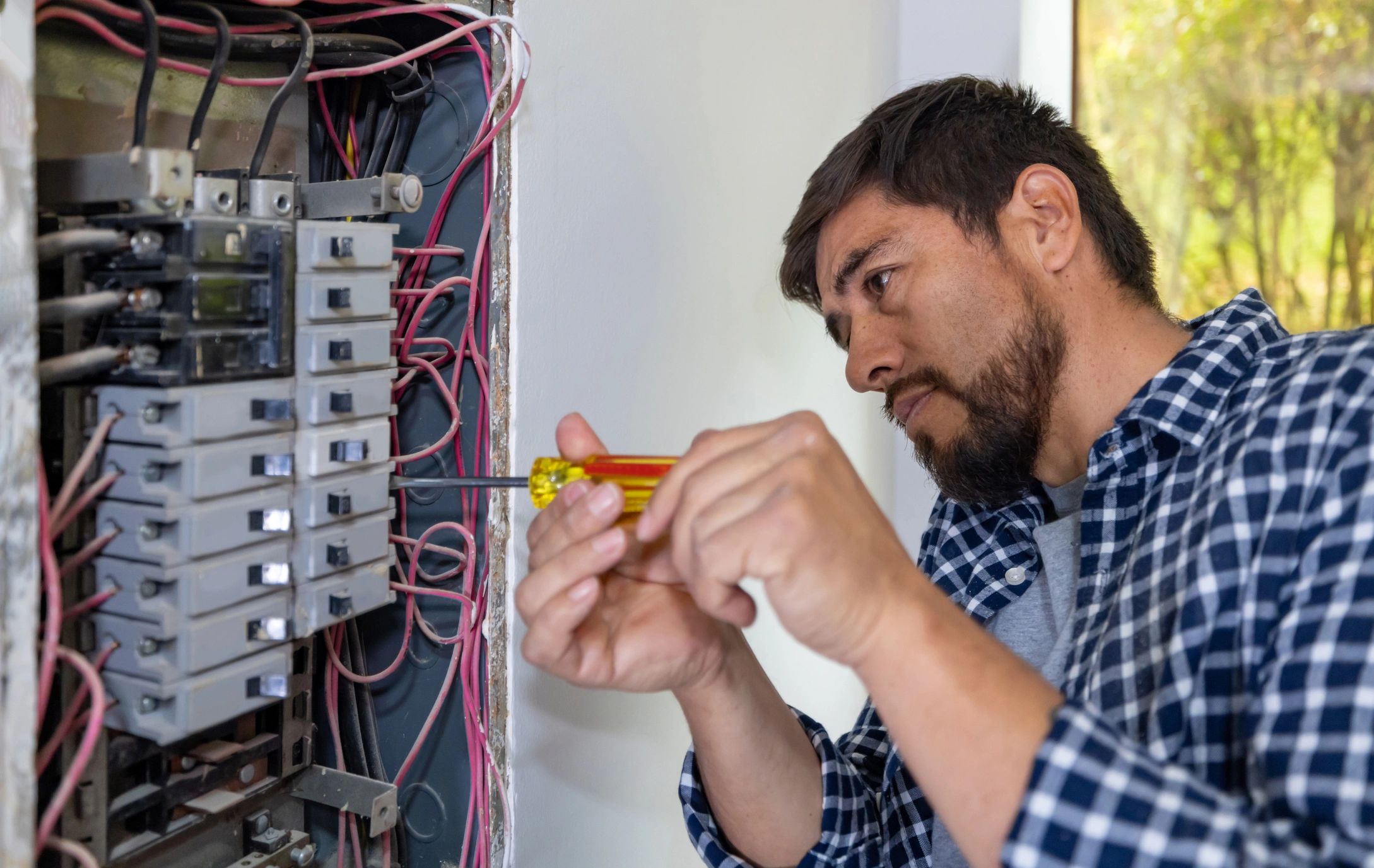 Electrician fixing a circuit breaker panel with a screwdriver.