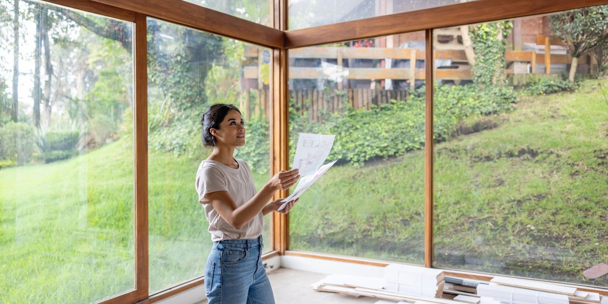 Woman examining architectural plans in a bright room with large glass windows.
