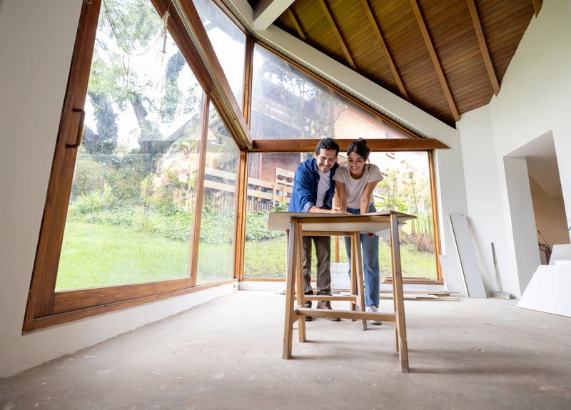 Happy Latin American couple renovating their house and looking at the blueprints while sharing ideas