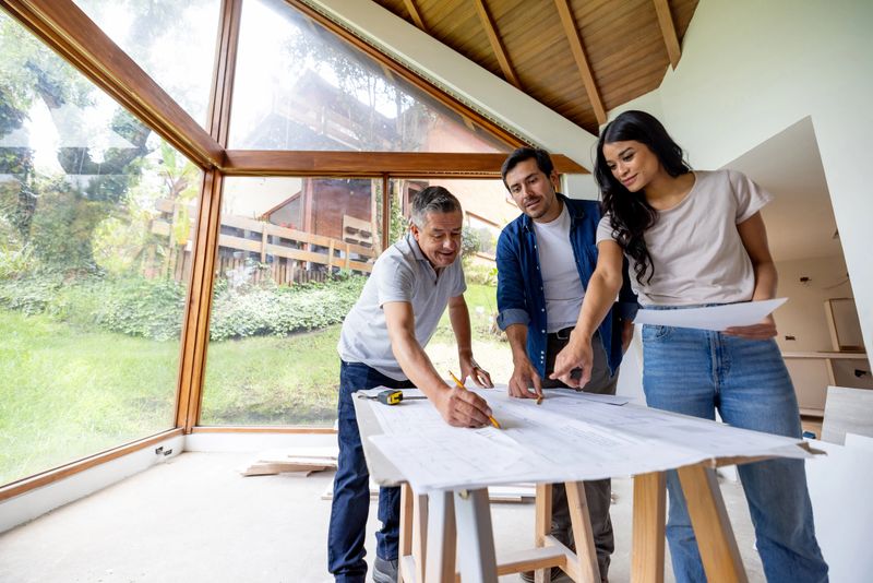 Latin American building contractor looking at blueprints with a couple remodeling their house