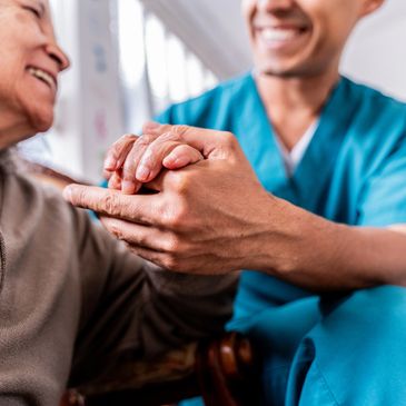 Healthcare worker holding elderly patient's hand with a smile.