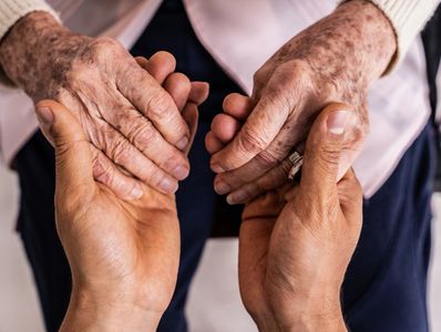 Younger hands gently holding elderly hands in a comforting gesture.
